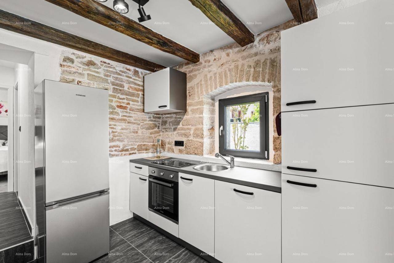 Moderne Küche mit weißen Schränken, dunkler Arbeitsplatte und integrierten Geräten, eingebettet in eine Steinwand.