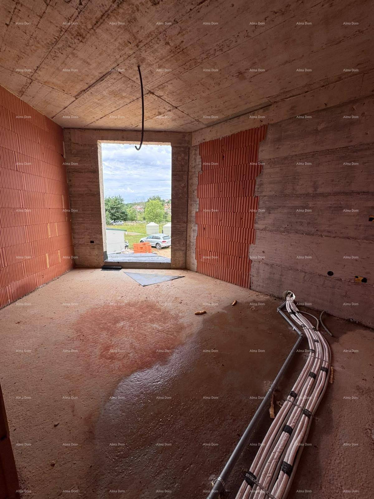 Rohbau eines Raumes mit großer Fensteröffnung und umfangreichen Leitungsinstallationen am Boden.