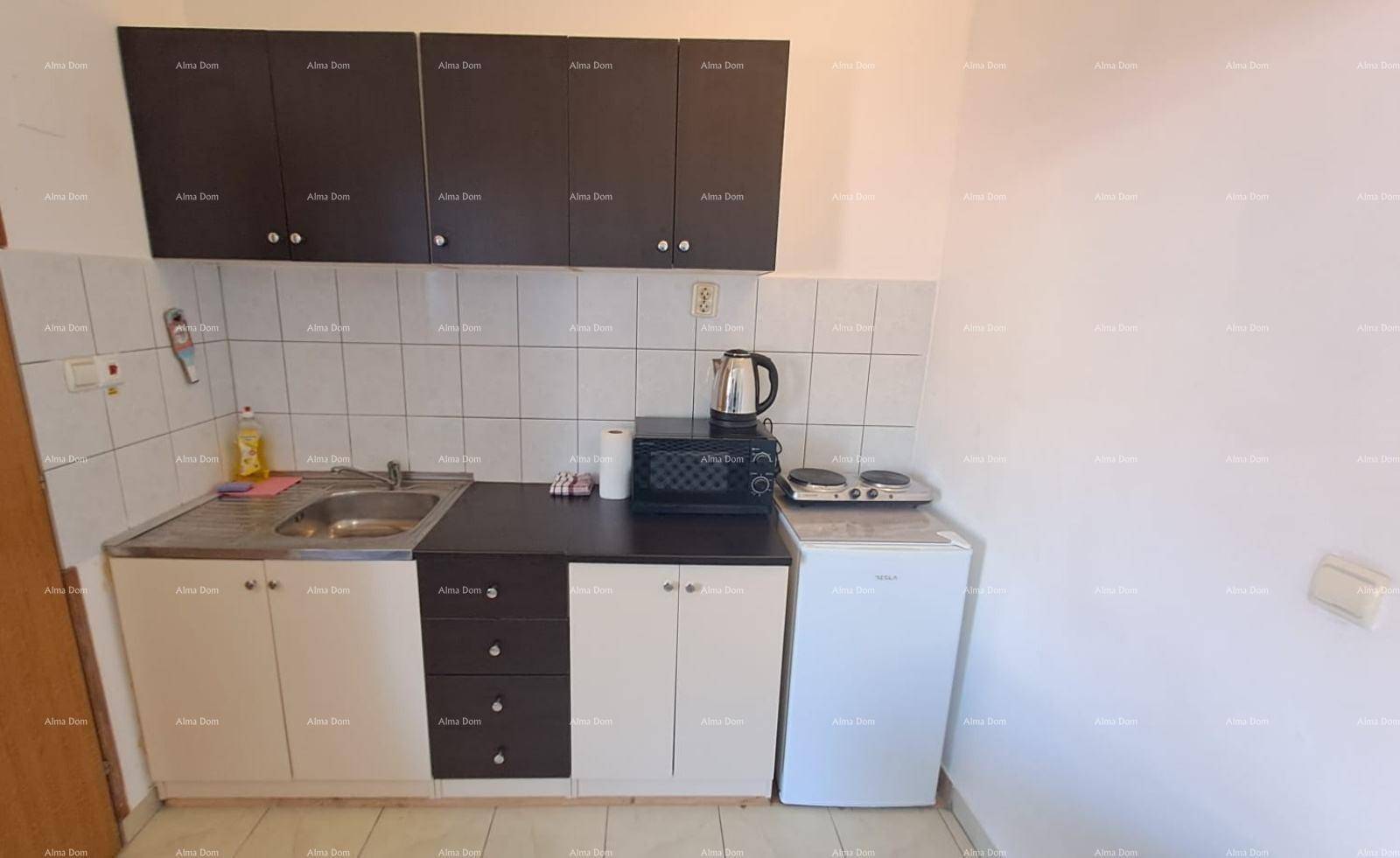 Kompakte Küchenzeile mit Spüle, Mikrowelle und Kochplatten, ausgestattet mit schwarzen und weißen Schränken.