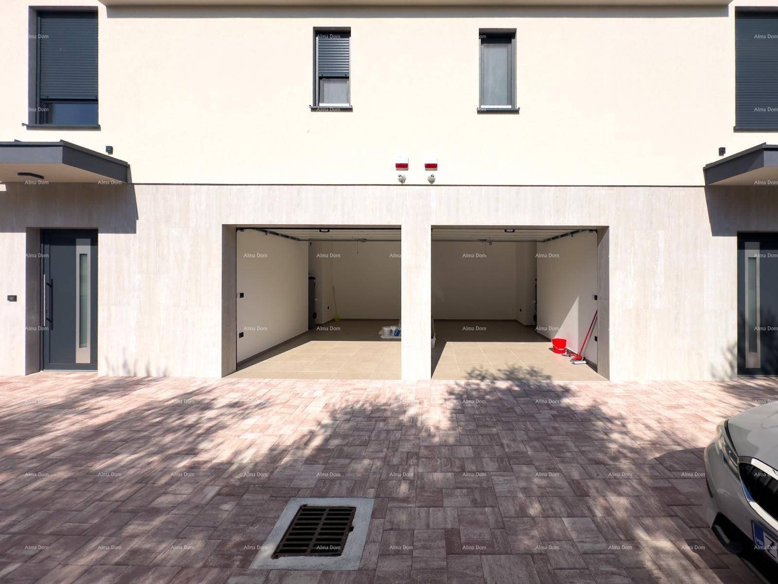 Vorderansicht des Gebäudes mit zwei offenen Garagentoren und einer breiten, gepflasterten Zufahrt.