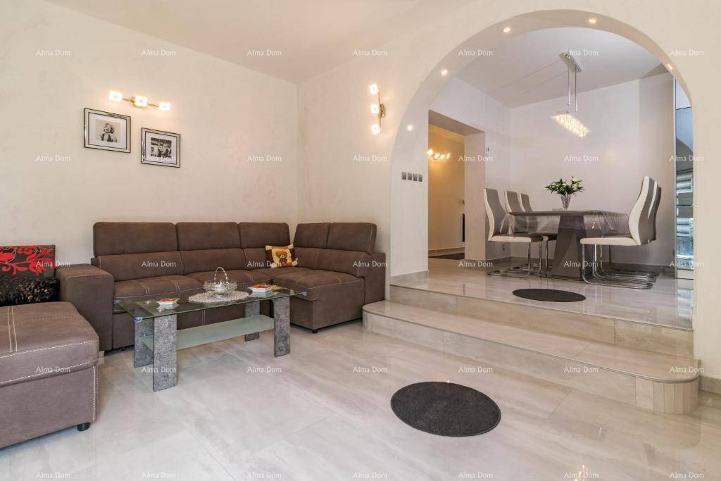 Gemütlicher Wohnbereich mit braunem Sofa und erhöhtem Essbereich, verbunden durch einen eleganten Bogen.