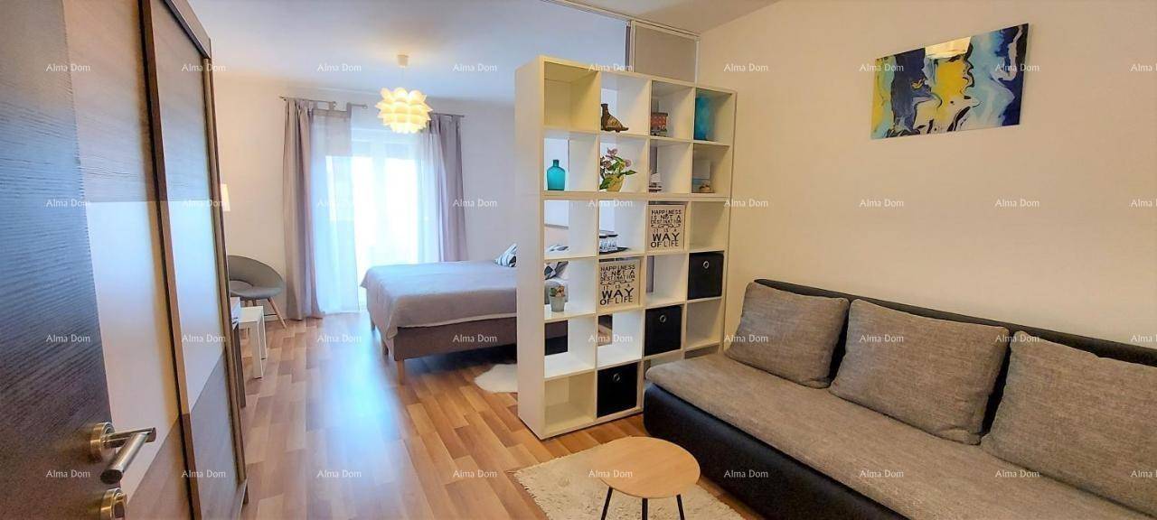 Wohnbereich mit Sofa und Regal als Raumteiler, angrenzend an einen Schlafbereich.