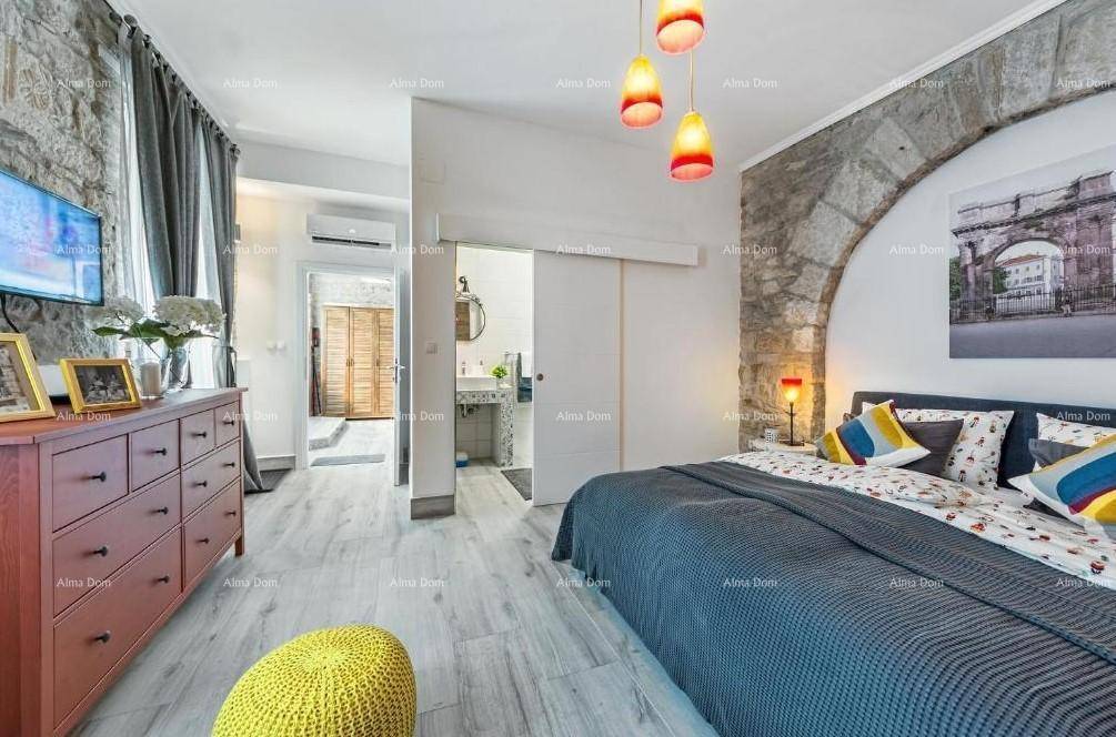 Schlafzimmer mit freigelegter Ziegelwand, Holzboden und Zugang zu einem angrenzenden Badezimmer.