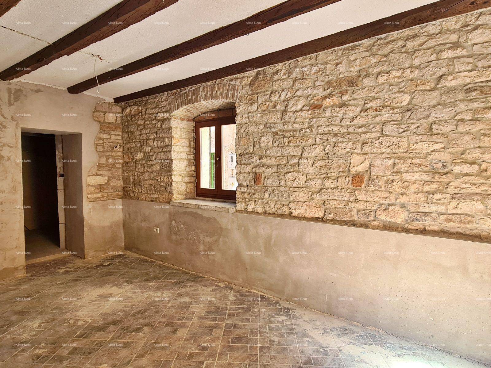 Wohnraum im Rohbau mit rustikaler Steinwand, Holzbalken und einem kleinen Fenster.