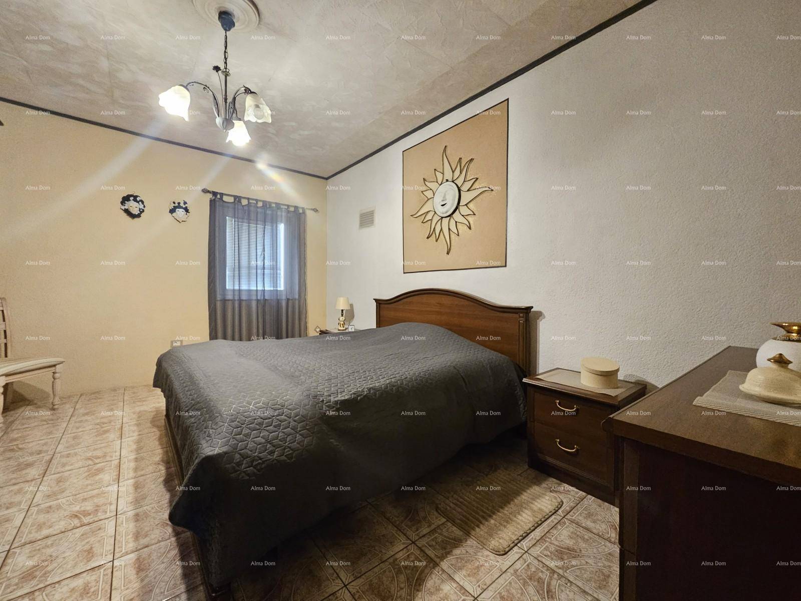 Schlafzimmer mit Doppelbett, Holzmöbeln und Fliesenboden, beleuchtet von einer Deckenleuchte.