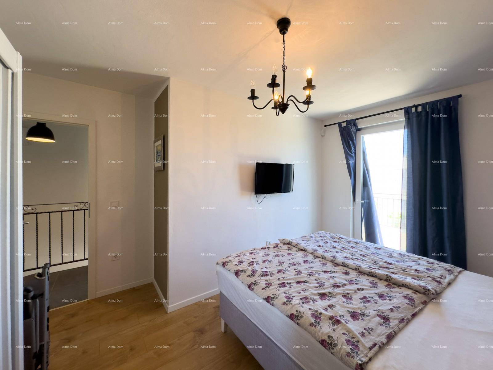 Helles Schlafzimmer mit Doppelbett, Fernseher und Zugang zum Flur mit Treppenhaus.