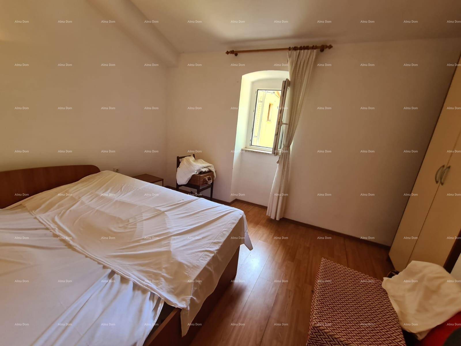Schlafzimmer mit Bett, Fenster mit Vorhängen und einem Kleiderschrank, auf Holzboden.
