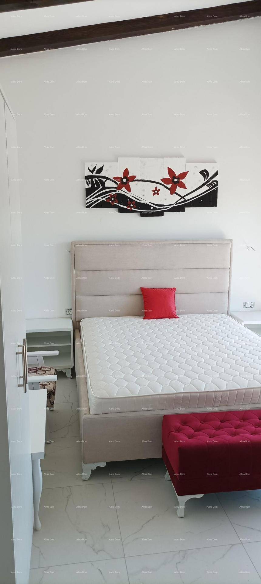 Schlafzimmer mit einem gepolsterten Bett, rotem Akzentkissen und moderner Wanddekoration.