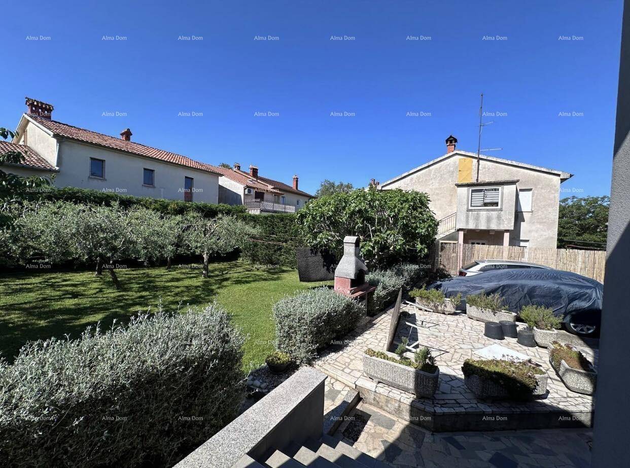 Weitläufiger Gartenbereich mit Rasen, Bäumen, einem Grillplatz und Blick auf Nachbarhäuser.