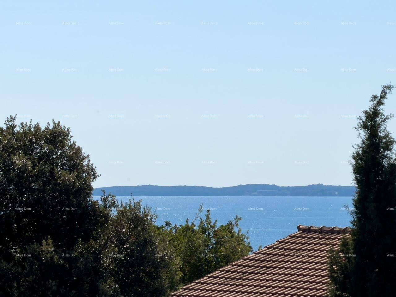 Panoramablick auf das Meer und die grüne Küstenlinie, umrahmt von Bäumen und einem Dach.