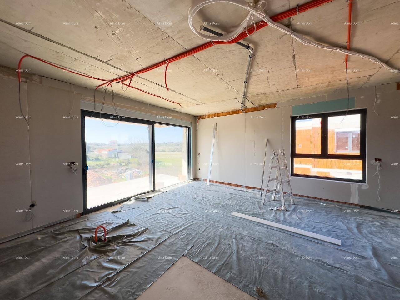 Innenraum im Rohbau mit sichtbaren Installationen, großen Fenstern und Blick ins Grüne.