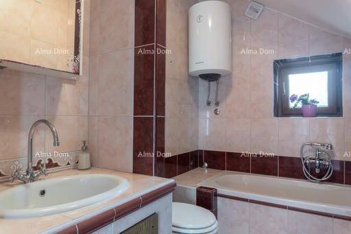 Badezimmer mit Badewanne, Waschbecken und Boiler, gefliest in Rosa- und Brauntönen unter Dachschräge.