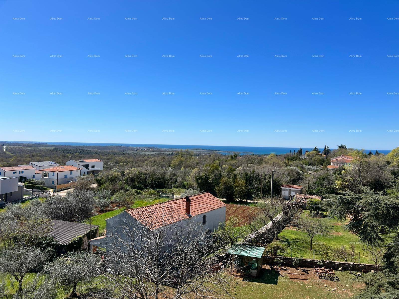 Weitläufige Landschaftsaufnahme mit Häusern, viel Grün und dem Meer am Horizont unter blauem Himmel.