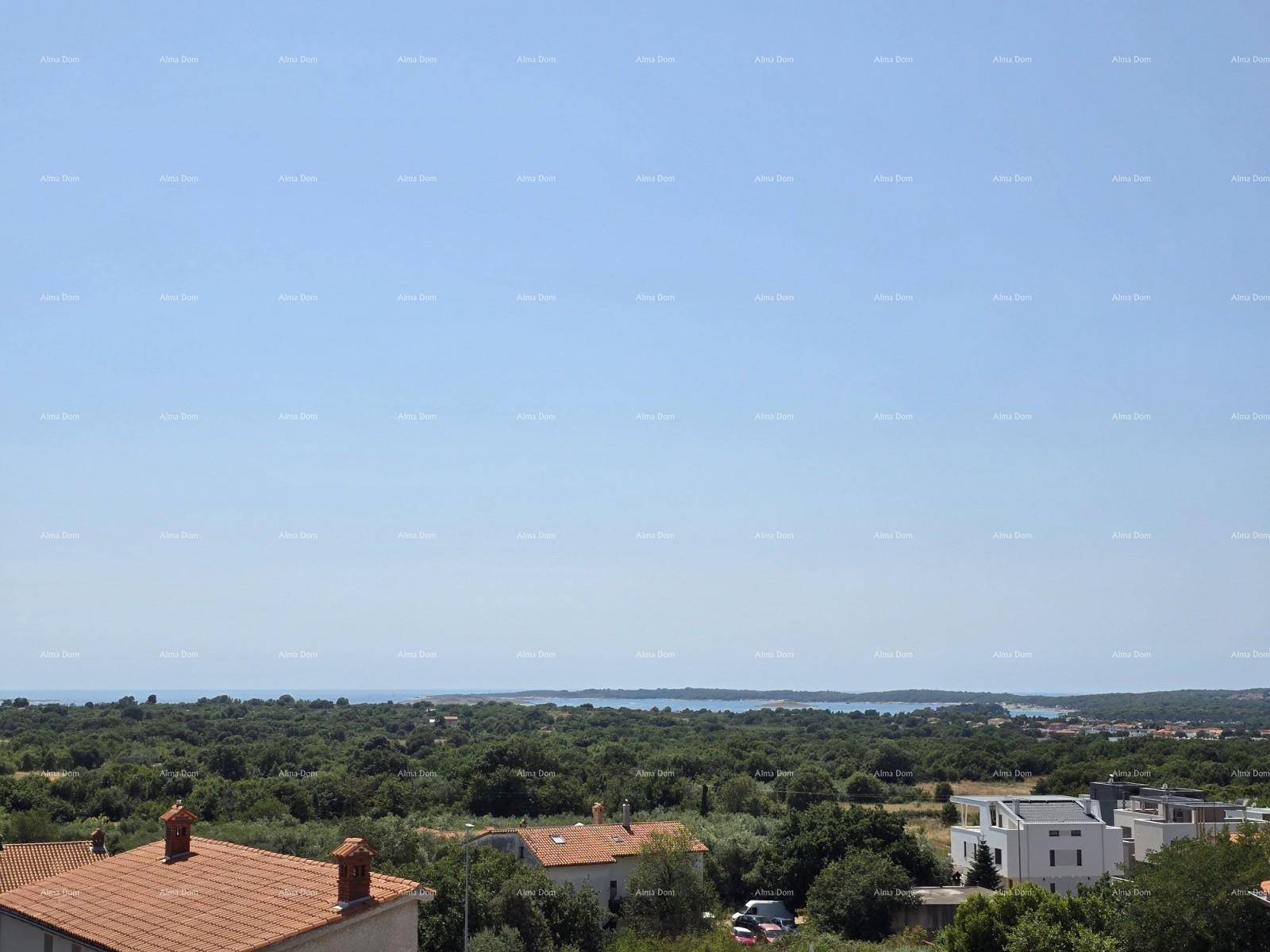 Weiter Blick über eine grüne Landschaft mit Dächern und dem Meer im Hintergrund unter klarem Himmel.