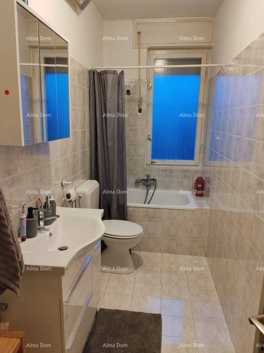 Gefliestes Badezimmer mit Badewanne, Duschvorhang, WC und Fenster für natürliche Belüftung.