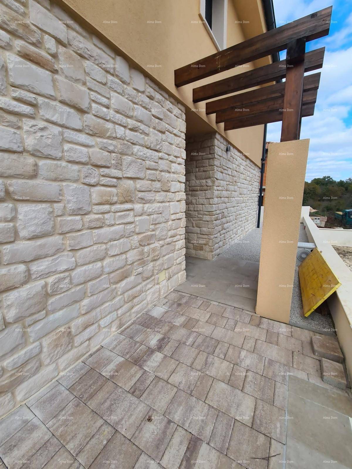Detailansicht der Natursteinfassade mit Holzbalken einer Pergola und gepflastertem Weg.