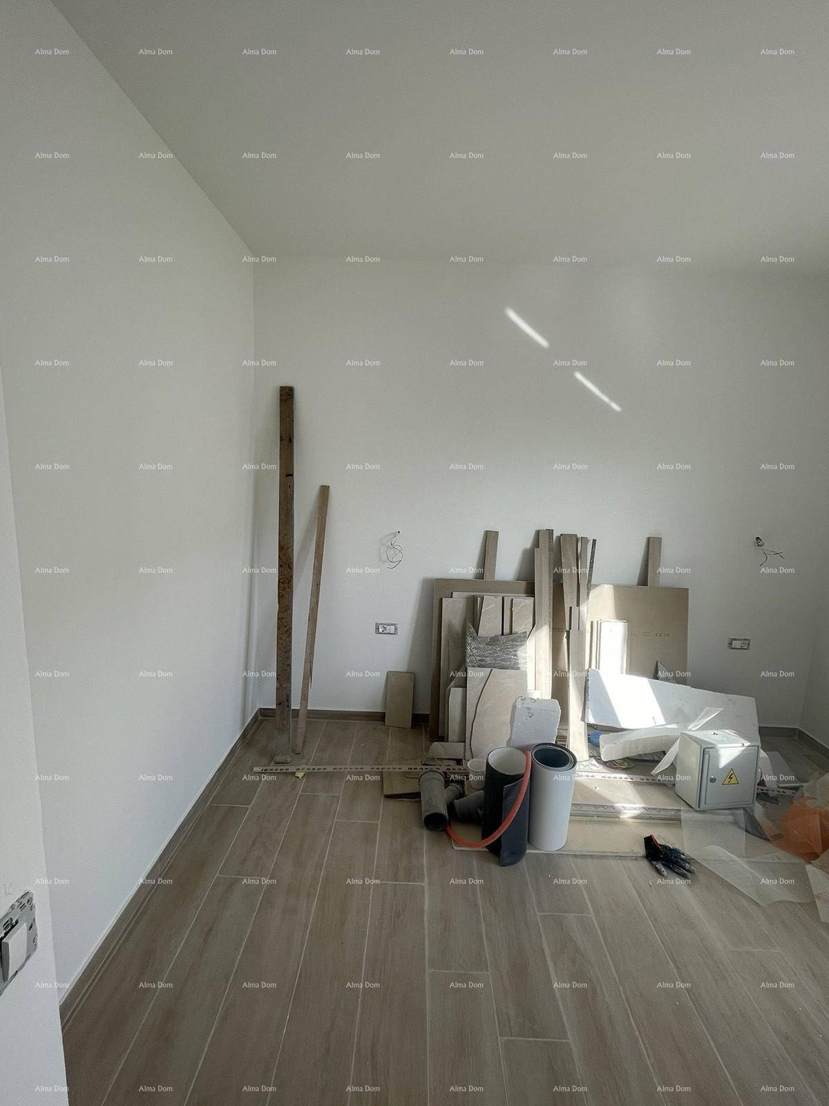 Unfertiges Zimmer mit Fliesenboden, weißen Wänden und gestapelten Baumaterialien.