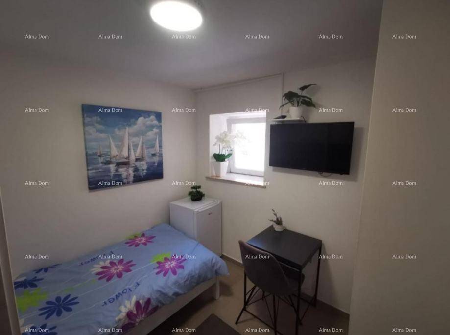 Kleines Schlafzimmer mit Einzelbett, Schreibtisch, Minikühlschrank und Wandfernseher.