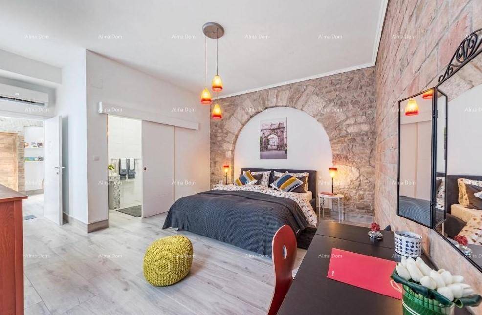 Schlafzimmer mit freigelegter Steinwand, Holzboden und Zugang zu einem angrenzenden Badezimmer.