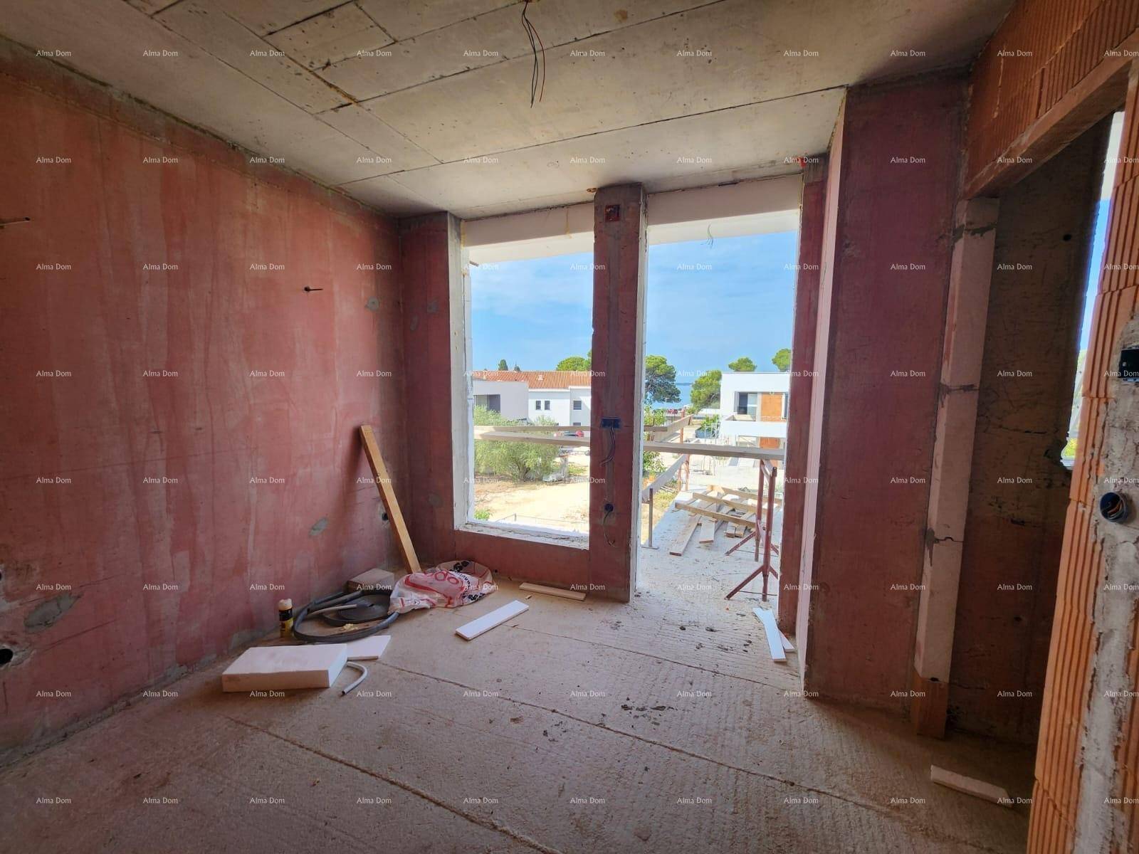 Rohbau eines Raumes mit großen Fensteröffnungen und Blick auf die Baustelle und das Meer.