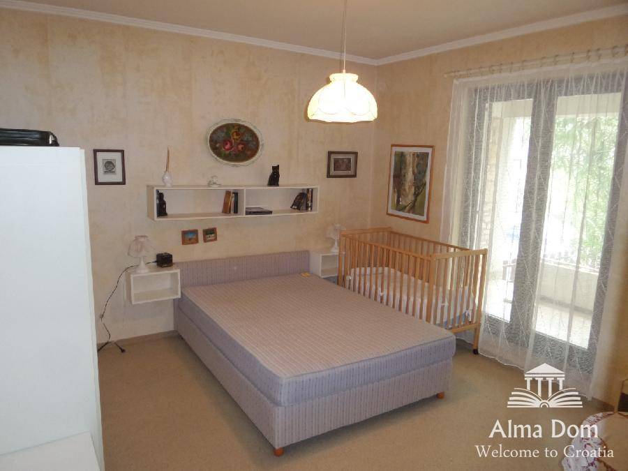 Schlafzimmer mit Doppelbett, Babybett und Zugang zu einem französischen Balkon, lichtdurchflutet.