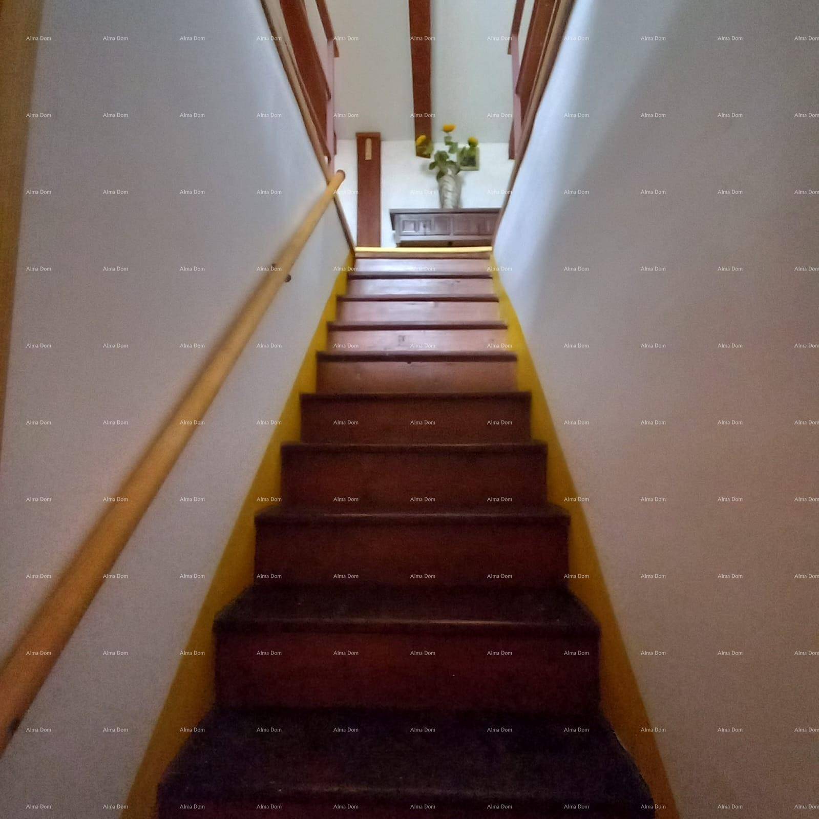 Holztreppe mit Geländer, die in ein oberes Stockwerk führt, unter sichtbaren Holzbalken.