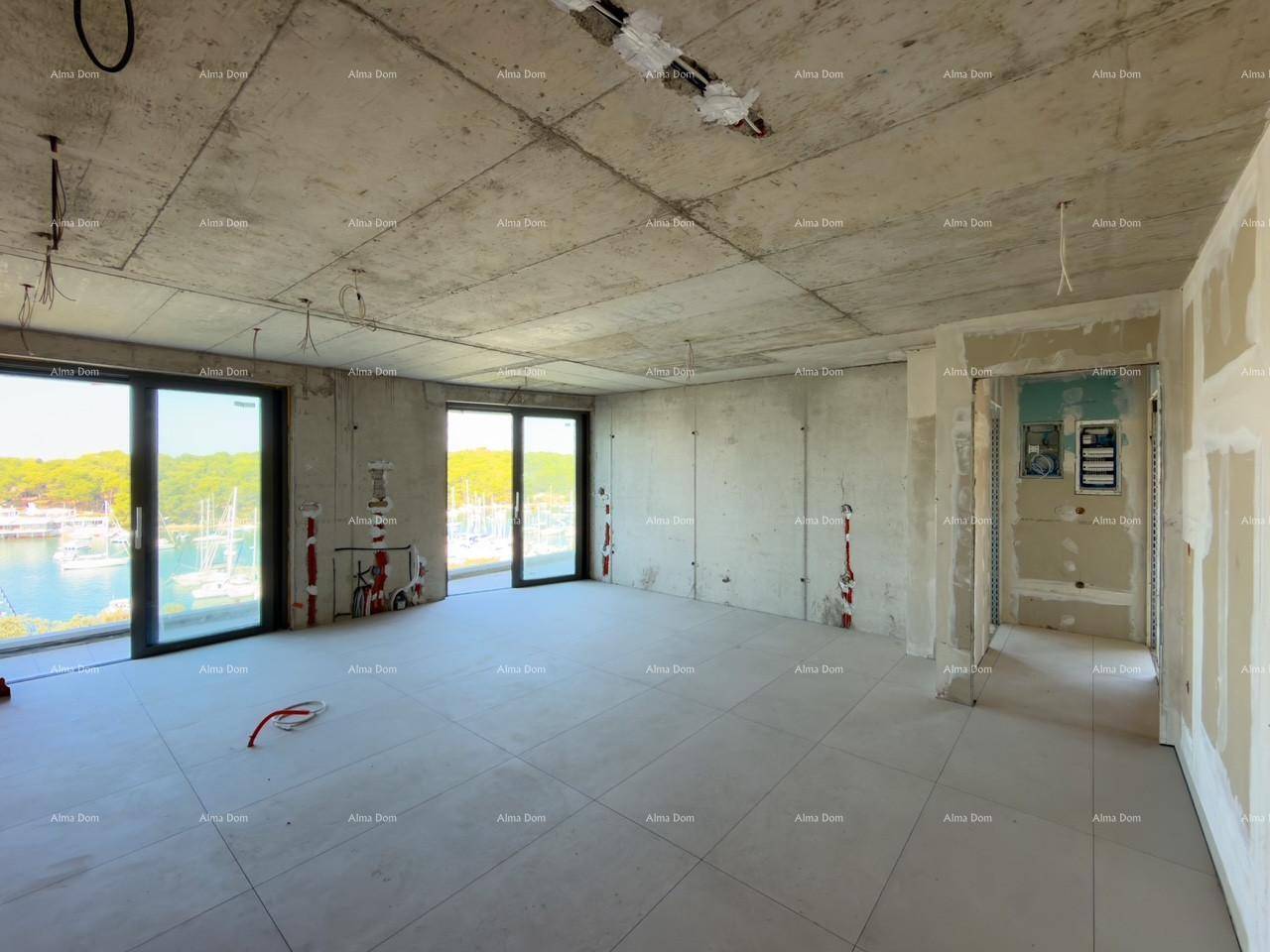 Großer Wohnraum im Rohbau mit Fliesenboden, Betondecke und großen Fenstern mit Blick auf den Yachthafen.