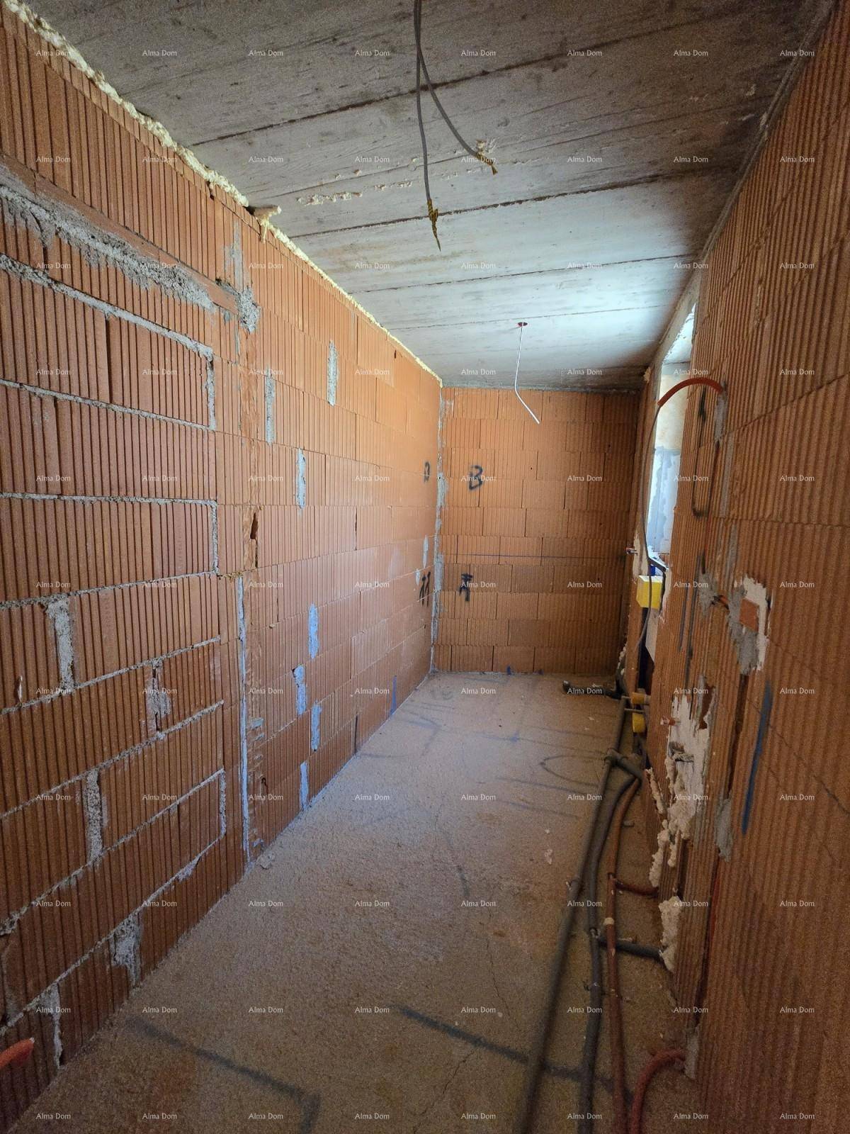 Schmaler Raum im Rohbau mit unverputzten Ziegelwänden und sichtbaren Leitungen an der Wand.