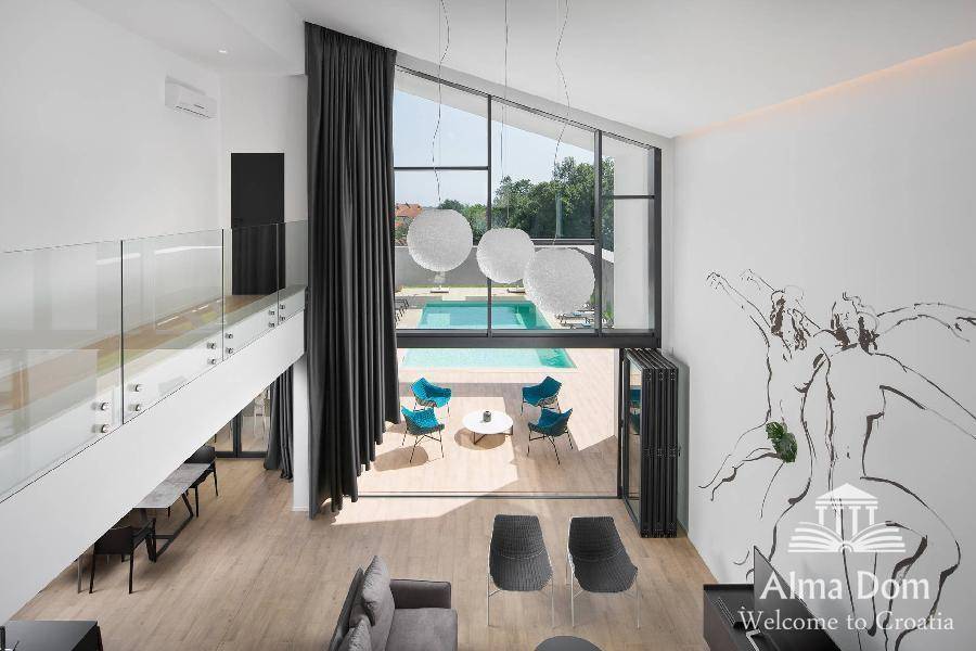 Blick von der Galerie in das Wohnzimmer mit hohen Fenstern und direktem Poolzugang.