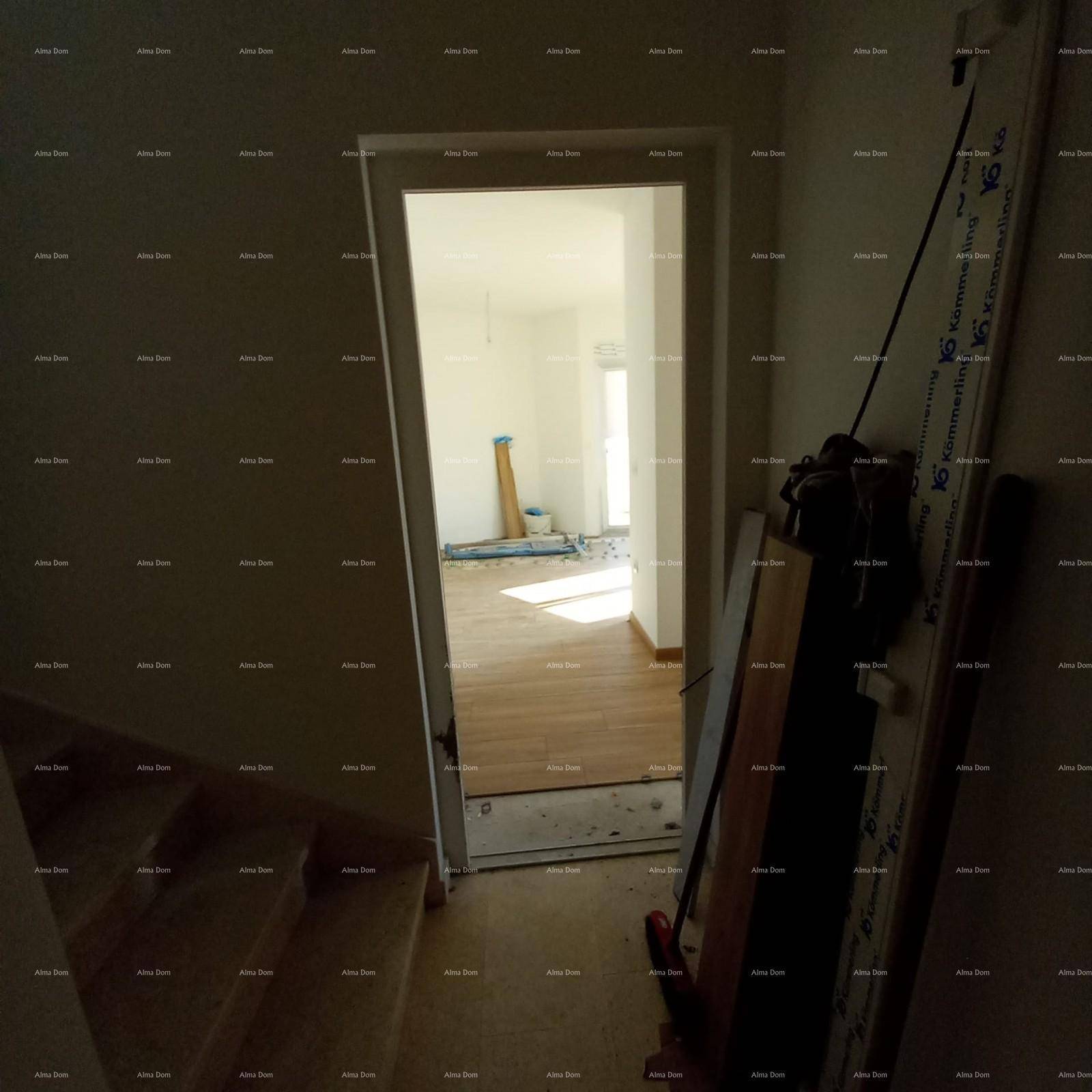 Offene Tür vom Treppenhaus in einen hellen Raum mit Holzboden und Tageslicht.