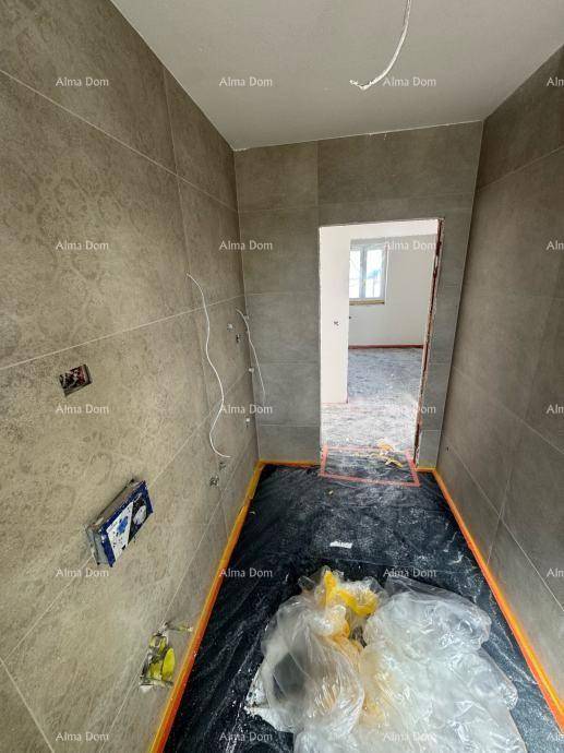 Unfertiges Badezimmer mit grauen Wandfliesen und Blick in einen angrenzenden, noch leeren Raum.