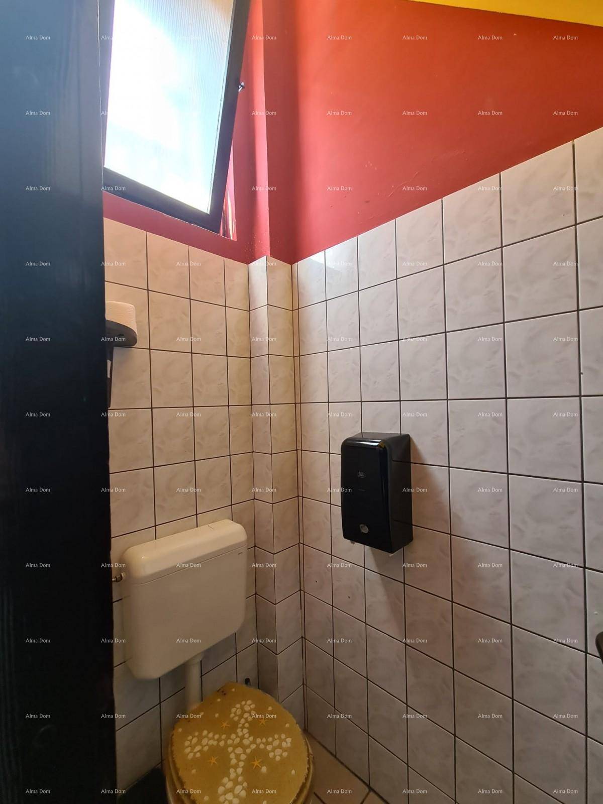 Kleine Toilette mit weißen Fliesen, einem Fenster und einem Toilettenspender an der Wand.