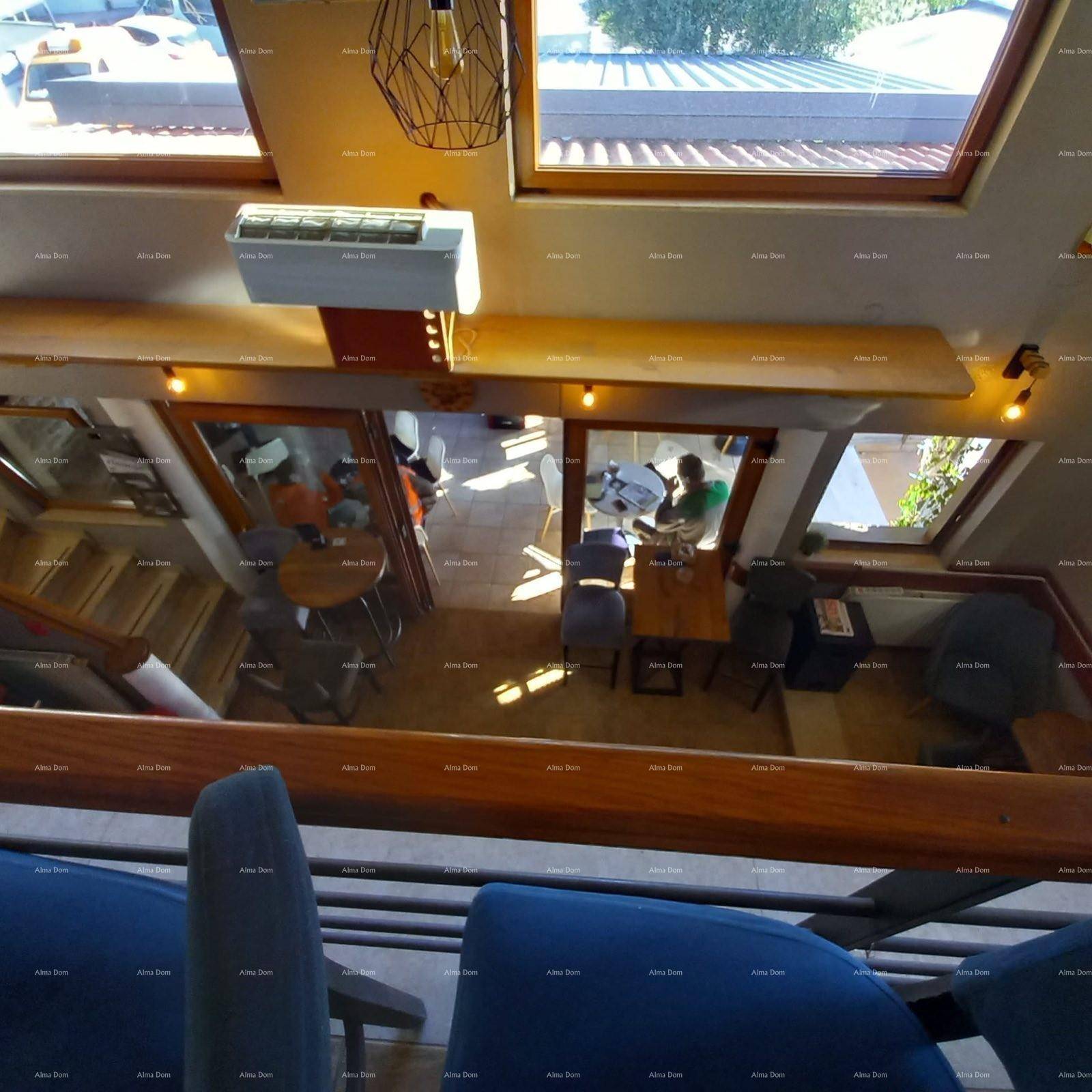 Blick vom Obergeschoss einer Bar auf den unteren Bereich mit Sitzgelegenheiten und großen Fenstern.
