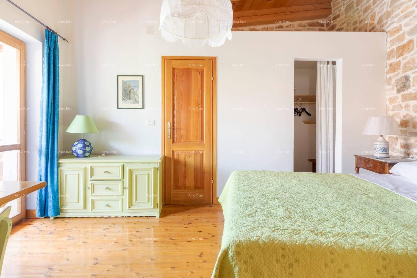 Helles Schlafzimmer mit Holzboden, Steinwand und einem Kleiderschrankbereich.