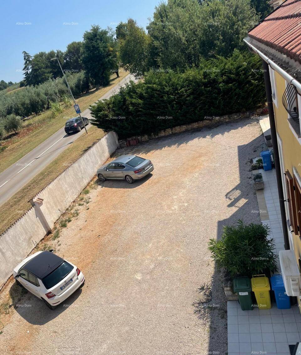 Außenparkplatz mit Kiesbelag neben einer Straße und einem Gebäude mit grünen Hecken.
