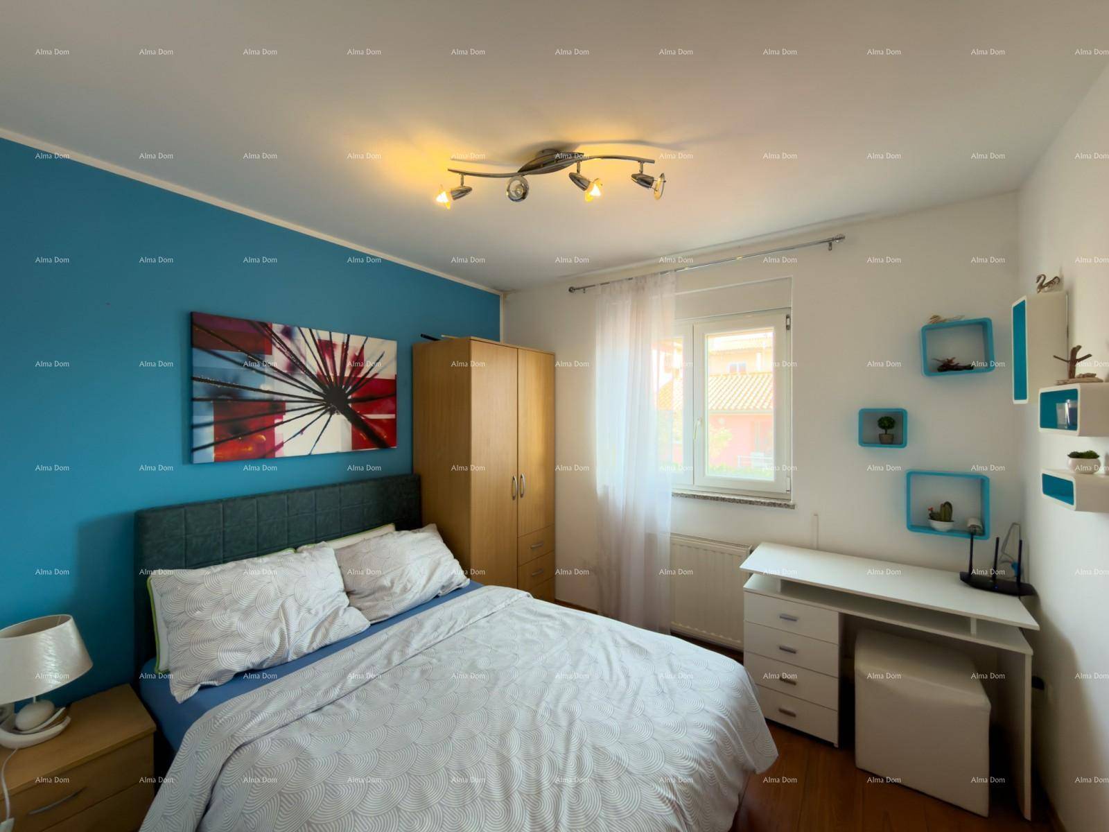 Schlafzimmer mit blauer Akzentwand, Doppelbett und Schreibtisch am Fenster.