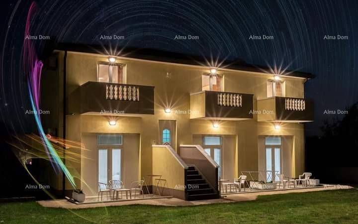 Beleuchtetes Haus bei Nacht mit mehreren Balkonen und Terrassen, umgeben von einem Garten.