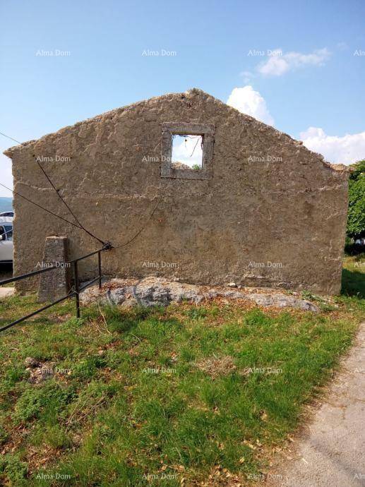 Rückseite eines verputzten Gebäudes mit einer leeren Fensteröffnung und Gras im Vordergrund.