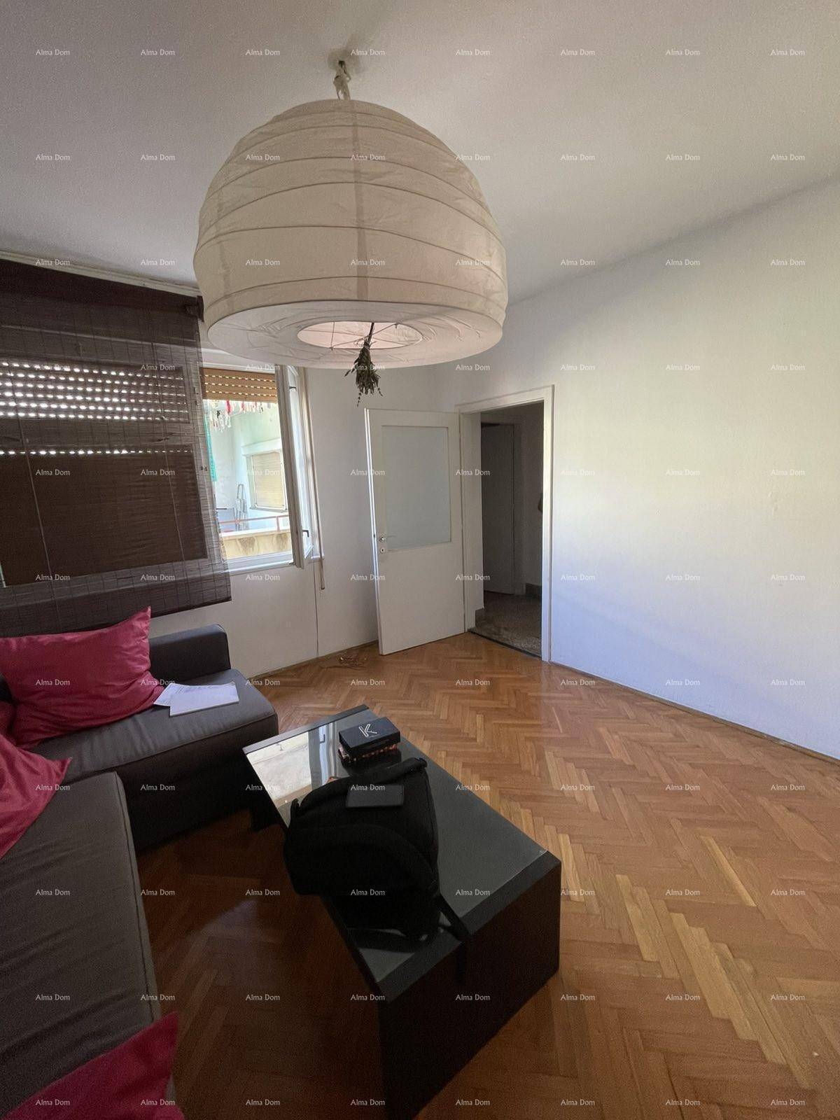Heller Wohnbereich mit Holzboden, Papierlampe und Zugang zu einem weiteren Raum.