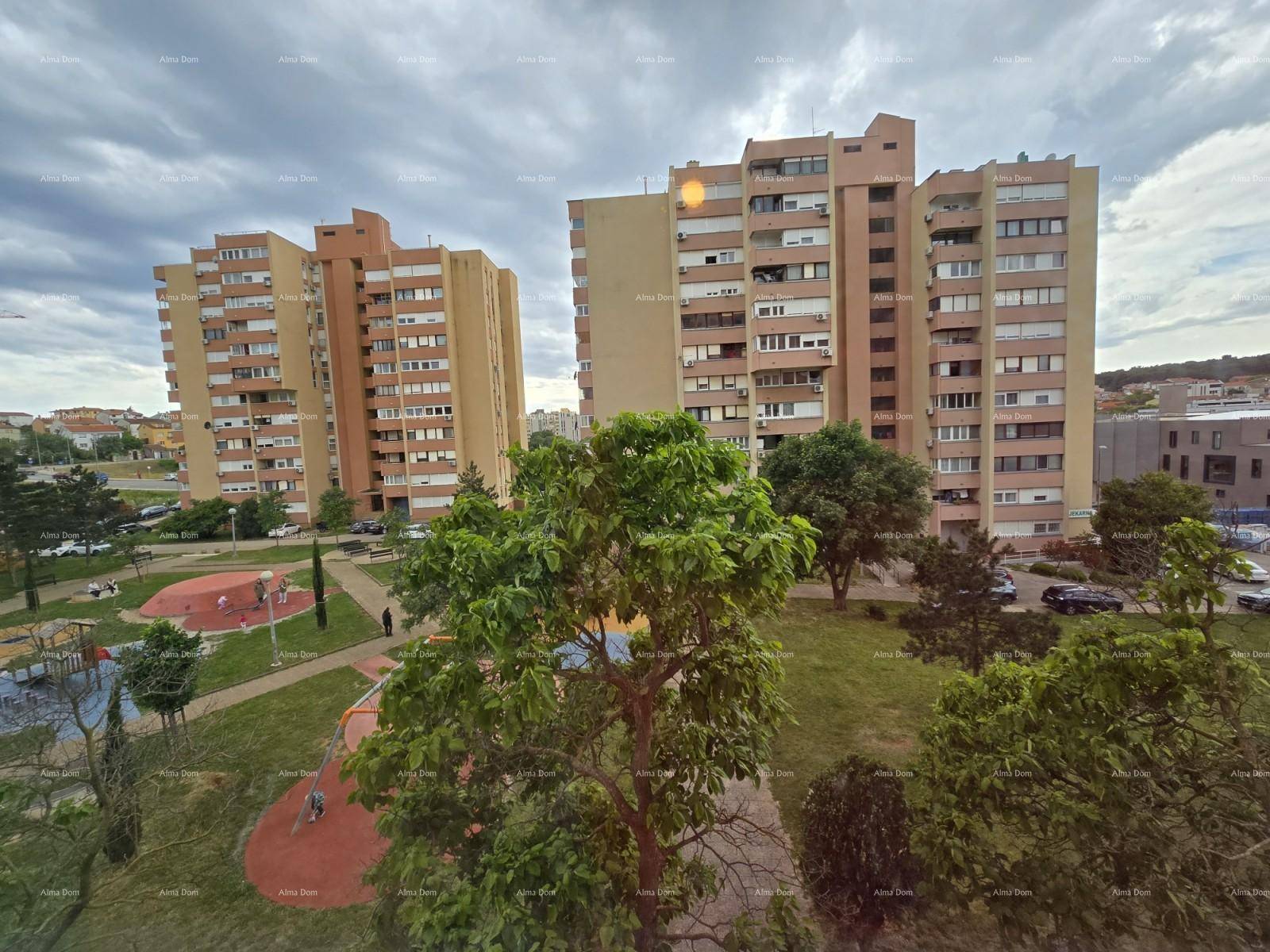 Blick auf Wohngebäude und einen Spielplatz mit Bäumen unter bewölktem Himmel.
