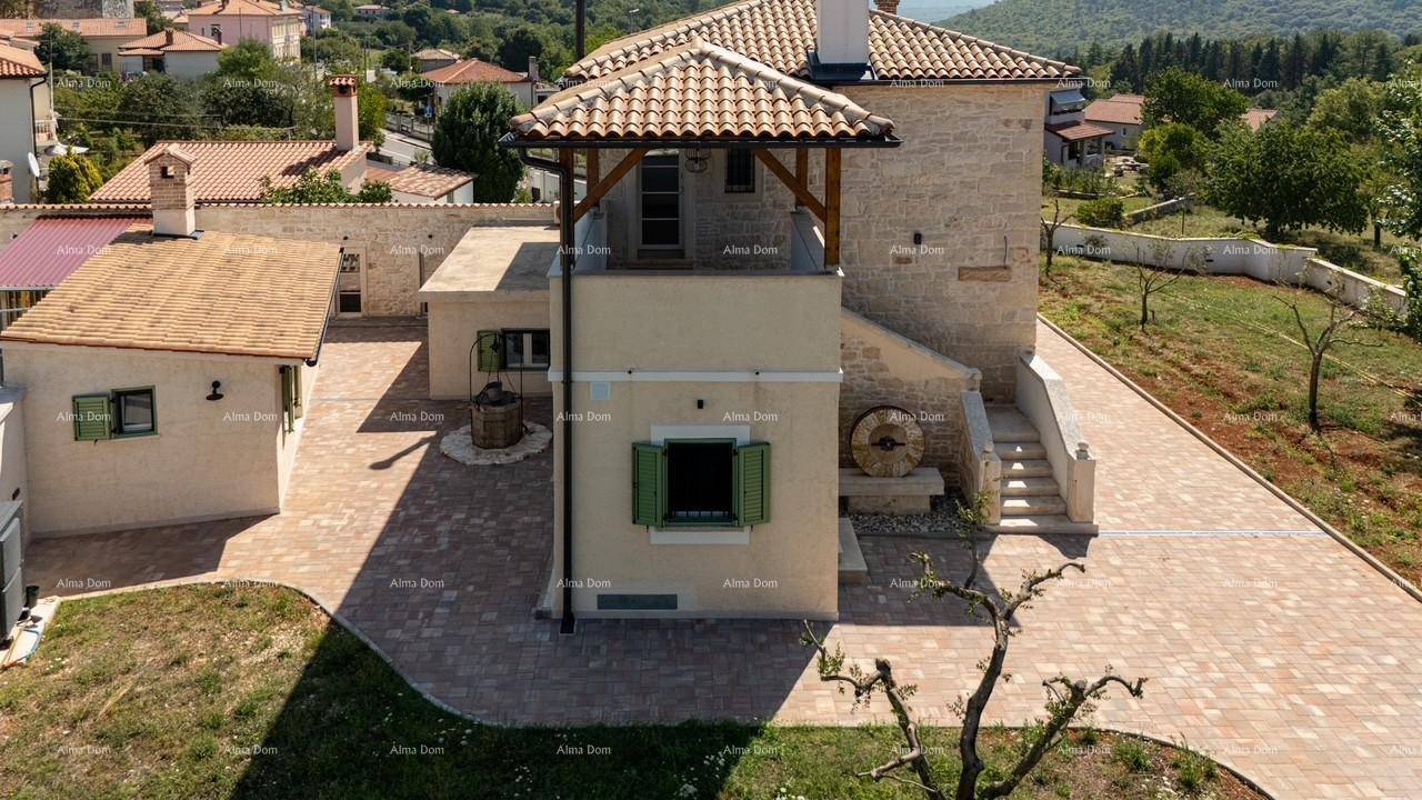 Seitenansicht des Steinhauses mit traditionellem Brunnen, einem überdachten Balkon und gepflasterter Zufahrt.