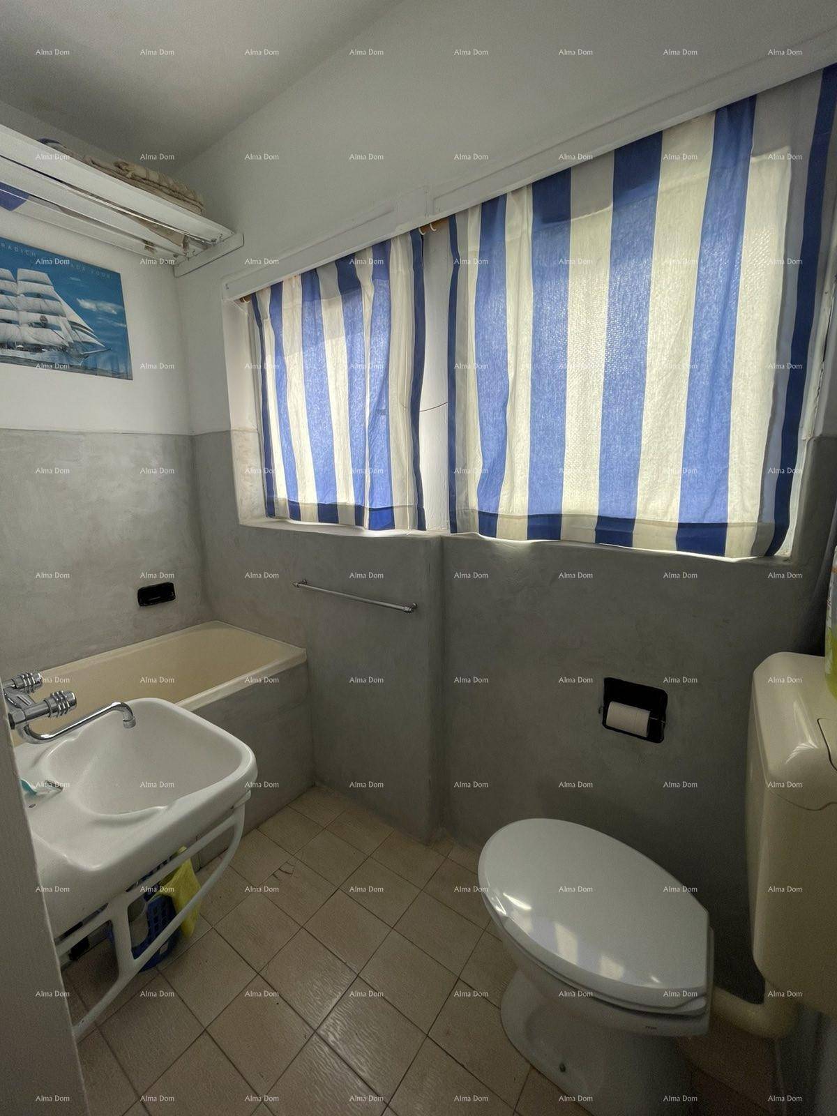Badezimmer mit Badewanne, Toilette und Waschbecken, mit gestreiften Vorhängen am Fenster.