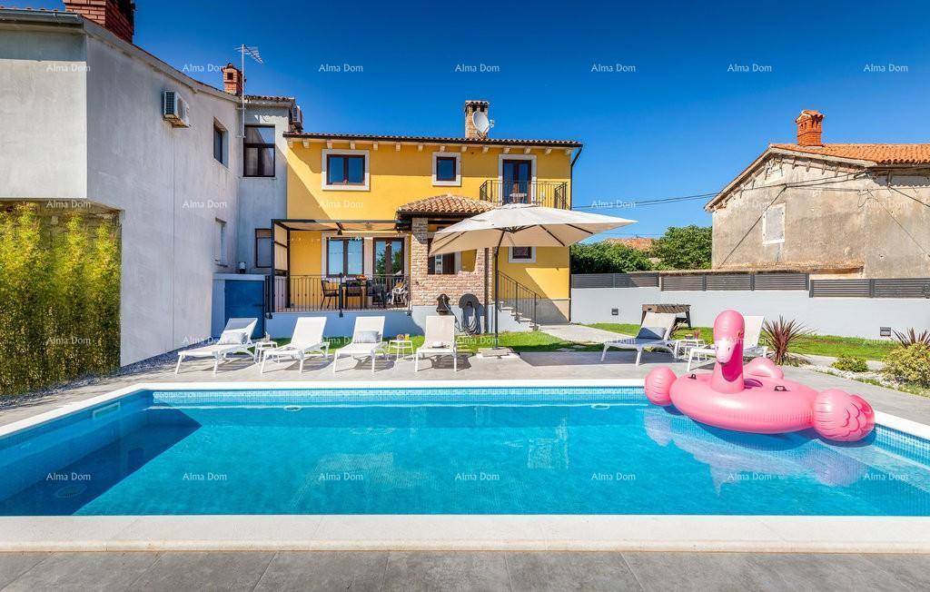 Ansicht des gelben Hauses vom Poolbereich aus mit Sonnenliegen und großem Sonnenschirm.