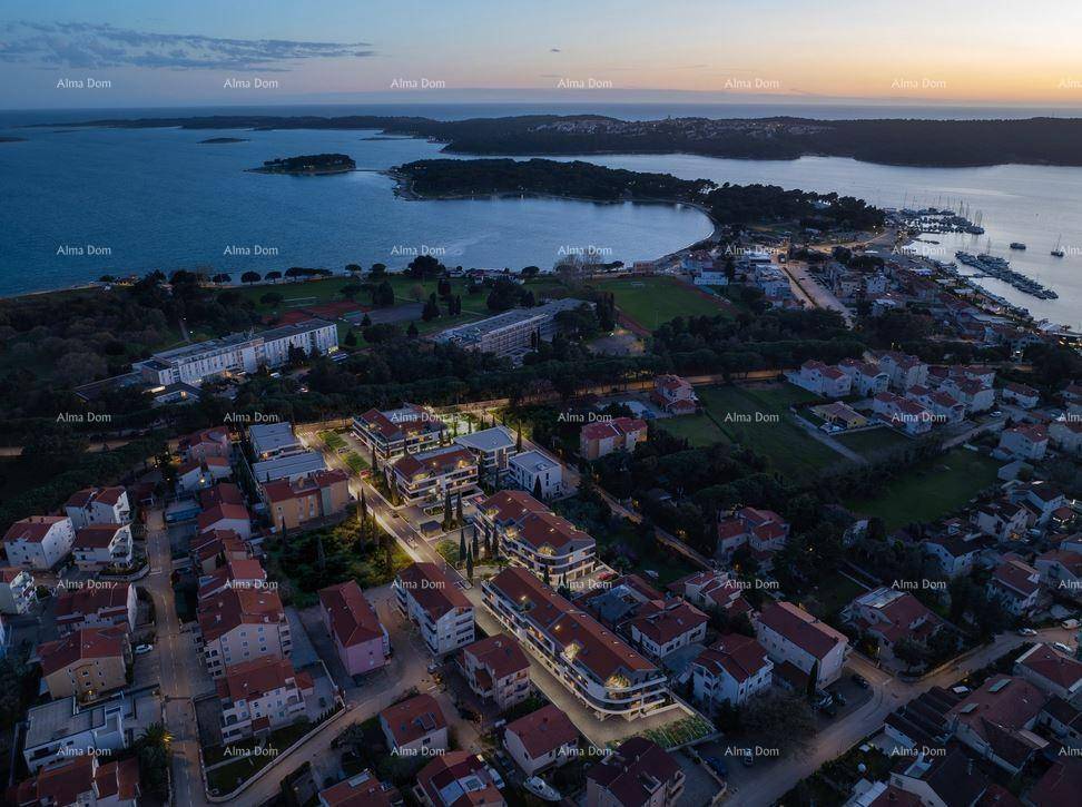 Abendliche Luftaufnahme des Wohnkomplexes mit beleuchteten Gebäuden und Blick auf die Bucht und Stadt.
