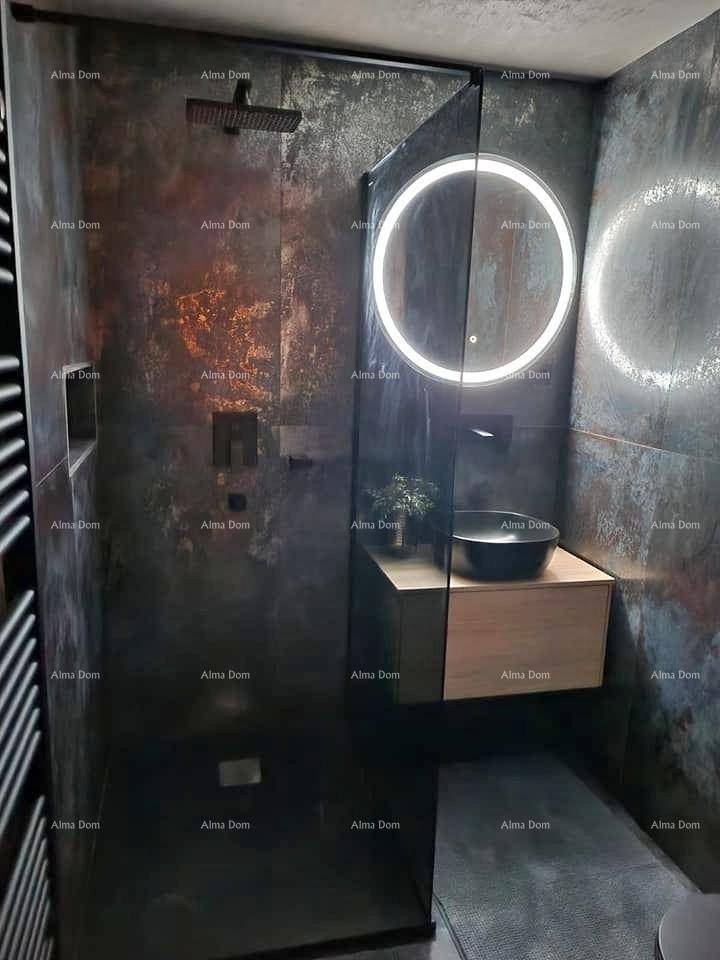 Modernes Badezimmer mit dunklen Fliesen, begehbarer Dusche und einem beleuchteten Spiegel über dem Waschbecken.