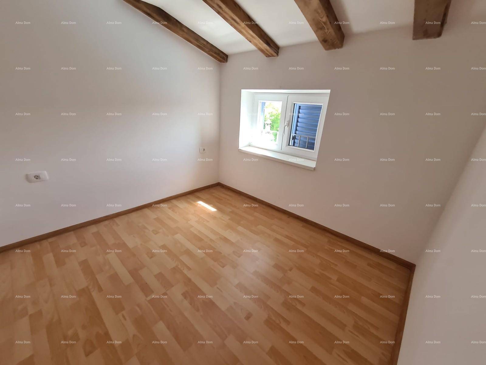 Leeres Zimmer mit Holzbalken an der Decke, Laminatboden und einem Fenster für natürliches Licht.