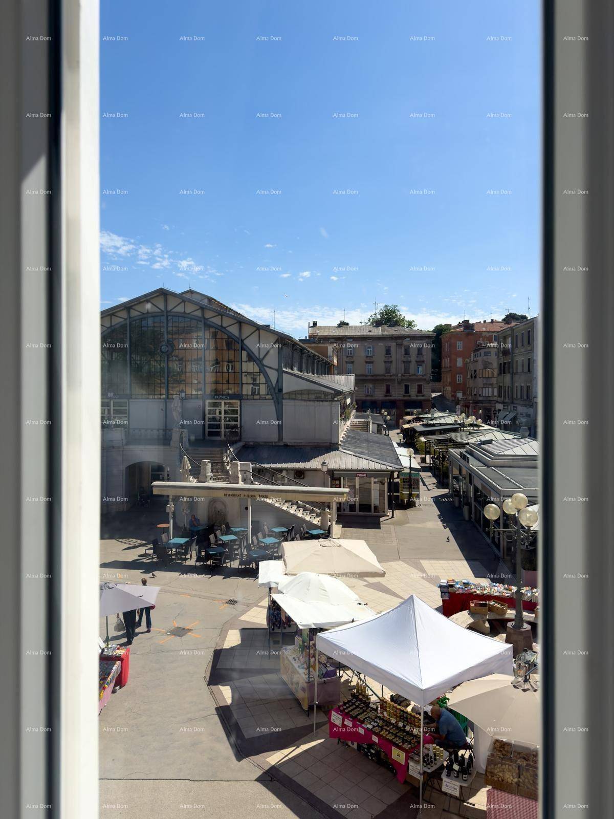 Blick aus dem Fenster auf einen lebhaften Stadtplatz mit Marktständen und historischer Architektur.