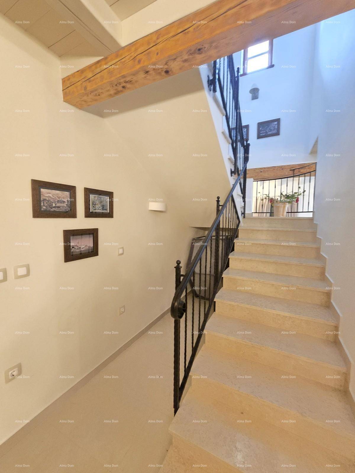 Helles Treppenhaus mit Steinstufen, schmiedeeisernem Geländer und sichtbaren Holzbalken.