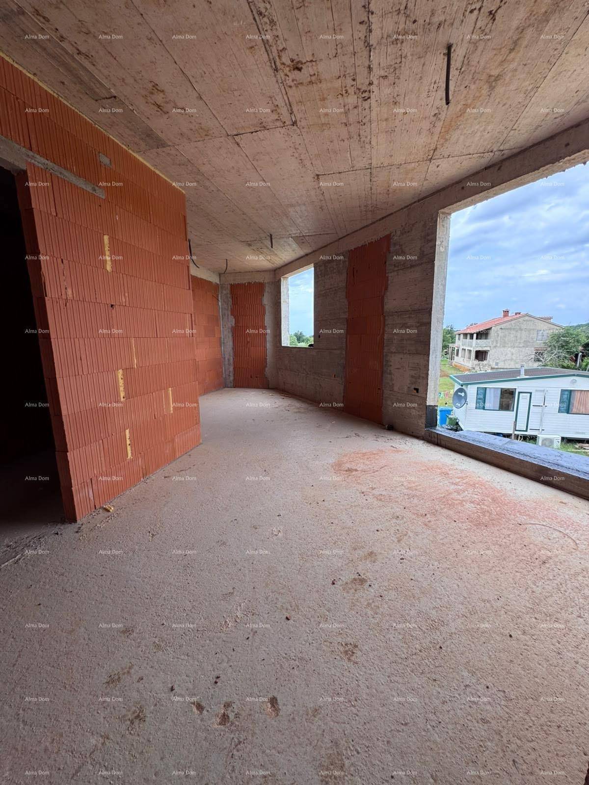 Rohbau eines Innenraums mit Ziegelwänden, Betonboden und großen Fensteröffnungen.