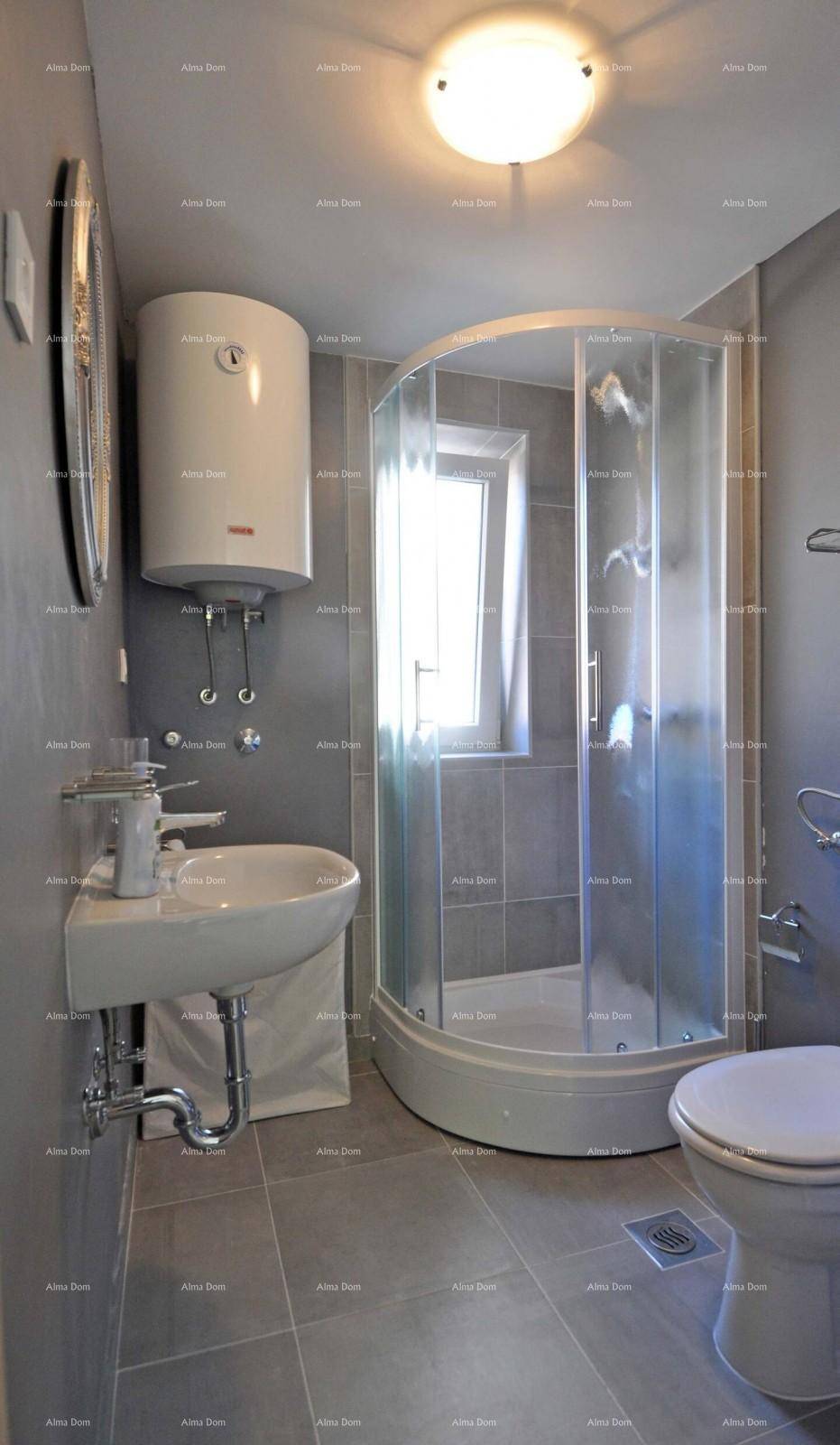 Kleines Badezimmer mit Duschkabine, Waschbecken, Toilette und Warmwasserboiler.